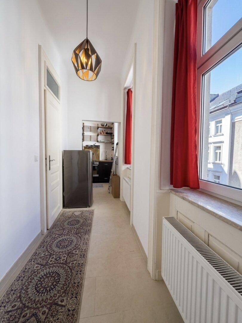 Langer Flur mit Fliesenboden, rotem Vorhang und Blick auf den Kühlschrank.
