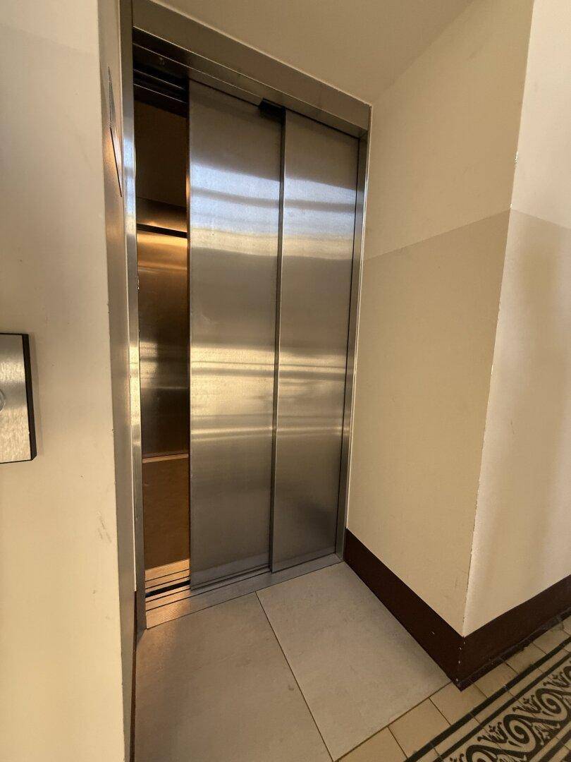 Moderner Aufzug mit Edelstahltüren in einem gepflegten Treppenhaus.