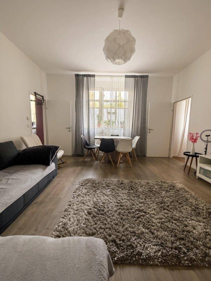 Geräumiger Wohn-Essbereich mit großem Fenster, viel Tageslicht und gemütlichem Teppich.
