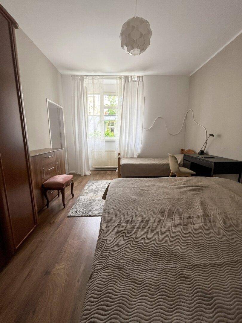 Helles Schlafzimmer mit zwei Einzelbetten, Schreibtisch und Fenster mit Vorhängen.