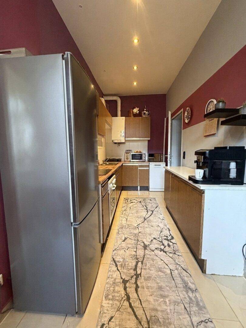 Schmale Küche mit Fliesenboden, Einbauschränken und großem Kühlschrank.