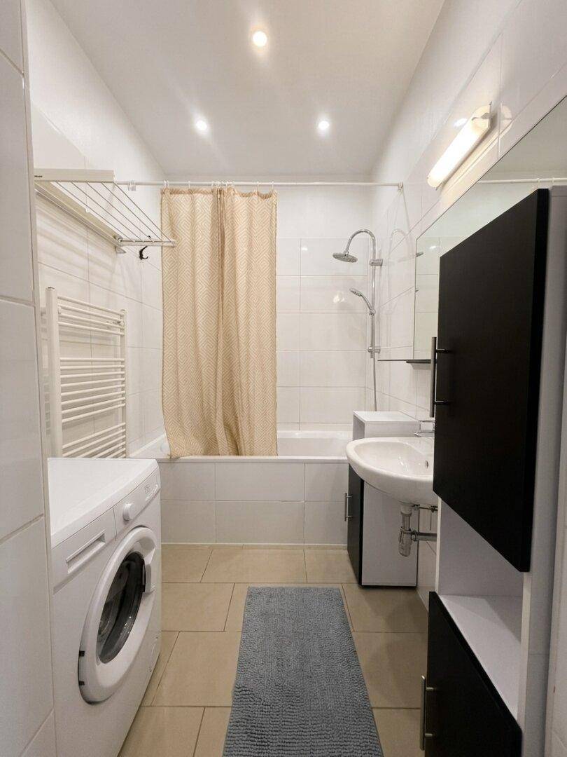 Modernes Badezimmer mit Badewanne, Dusche, Waschmaschine und weißen Fliesen.