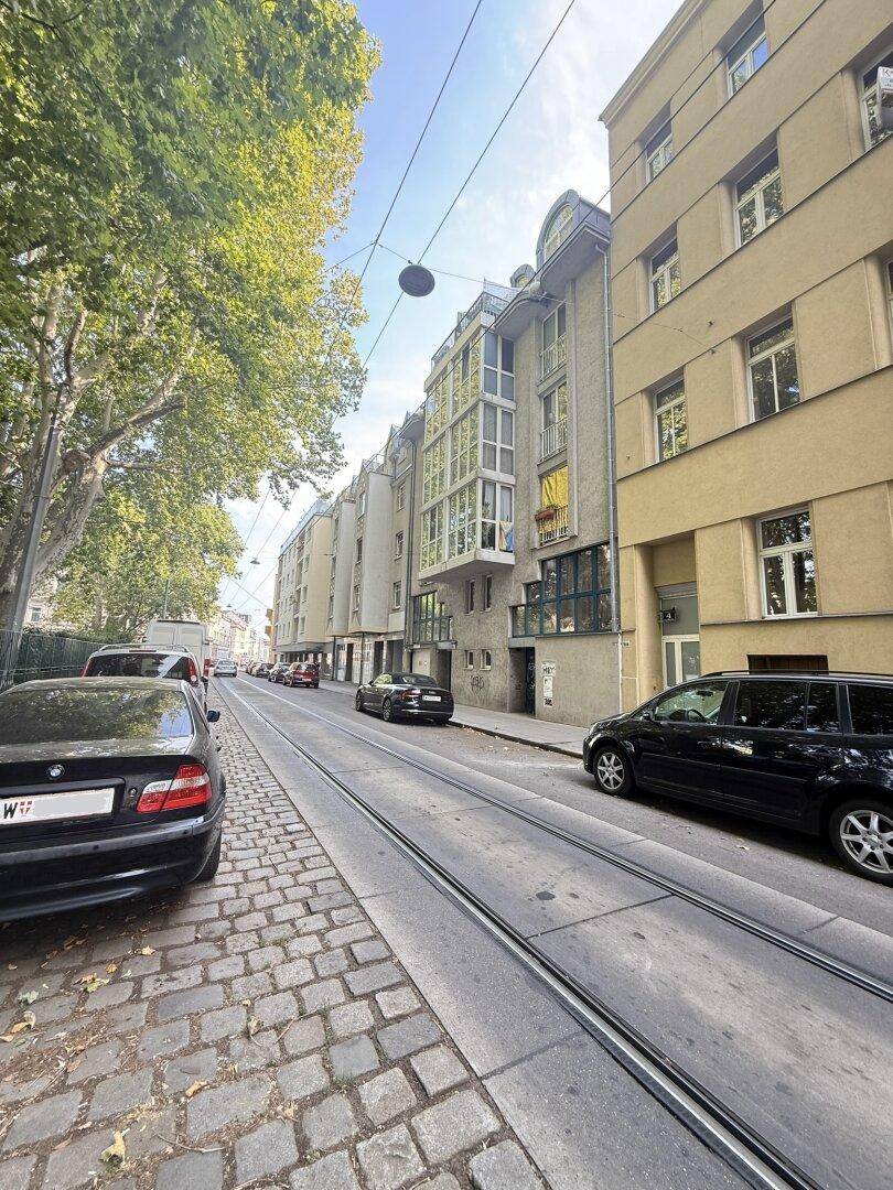Stadtansicht mit Gebäuden, Bäumen und Straßenbahnschienen, die das urbane Umfeld zeigen.