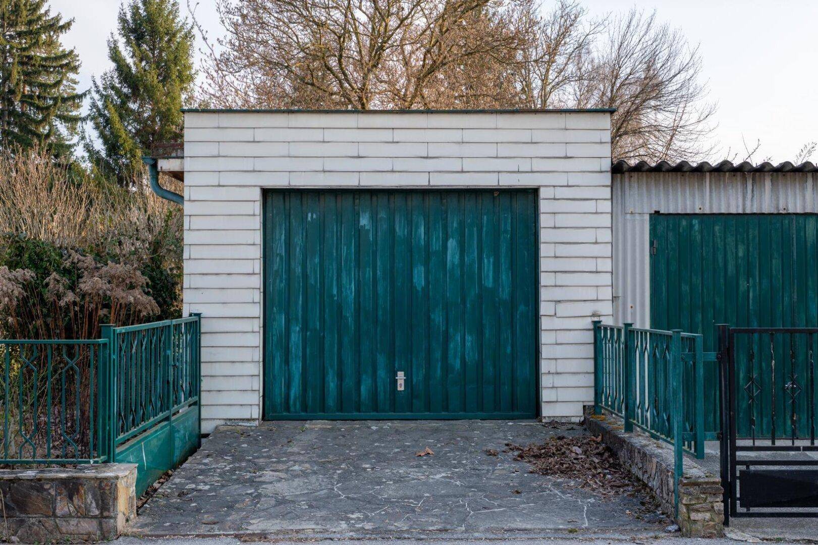 Eine alte Garage mit einer markanten grünen Holztür und weiß gestrichenen Ziegeln.