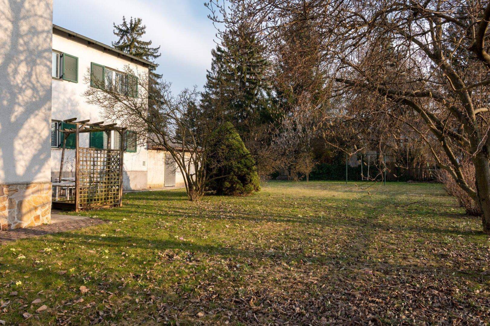 Großer Gartenbereich mit Rasenfläche, Bäumen und einem Teil der Hausfassade im Hintergrund.