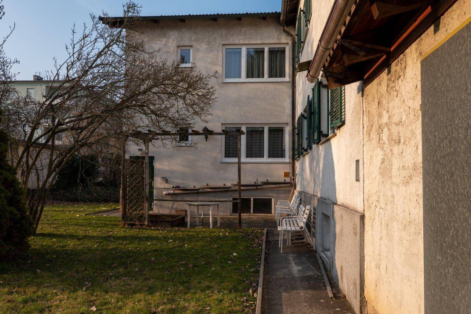 Seitenansicht des Hauses mit einem kleinen Sitzbereich und Blick in den Garten.