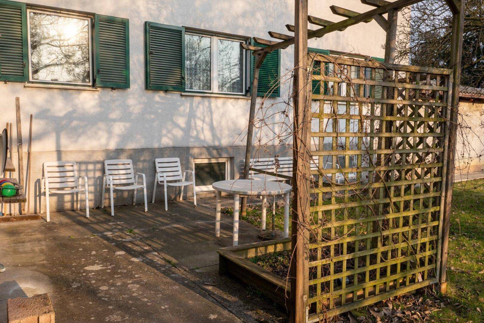 Kleine Terrasse mit Gartenmöbeln und einer Holzpergola, umgeben von Grün.