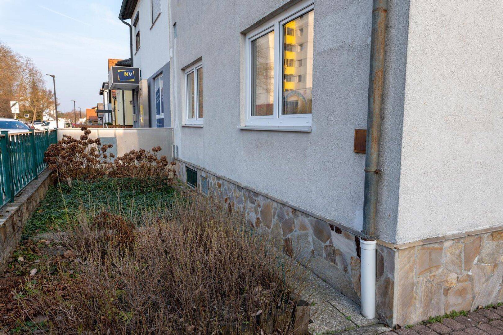 Seitenansicht der Hausfassade mit Natursteinverkleidung im unteren Bereich und einem kleinen Beet.