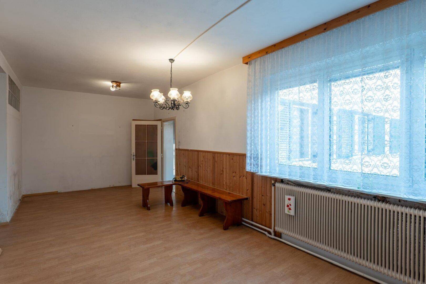 Wohnzimmer mit Laminatboden, Holzvertäfelung und einem Fenster mit Spitzenvorhängen.