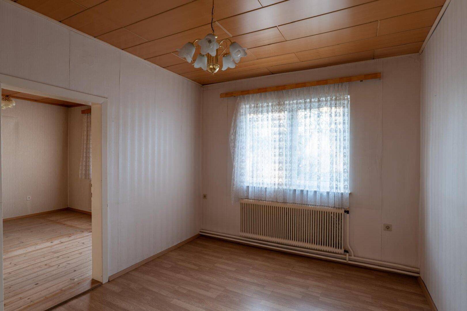 Schlafzimmer mit Laminatboden, Holzdecke und einem Fenster mit viel Tageslicht.