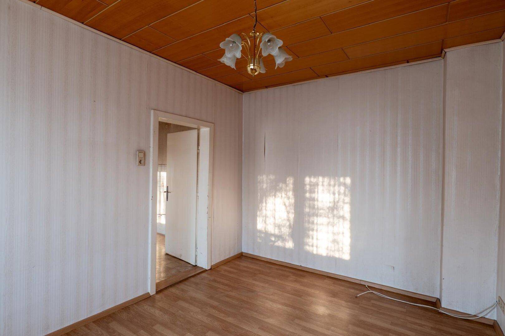 Helles Zimmer mit Laminatboden, Holzdecke und einem Durchgang zu einem weiteren Raum.