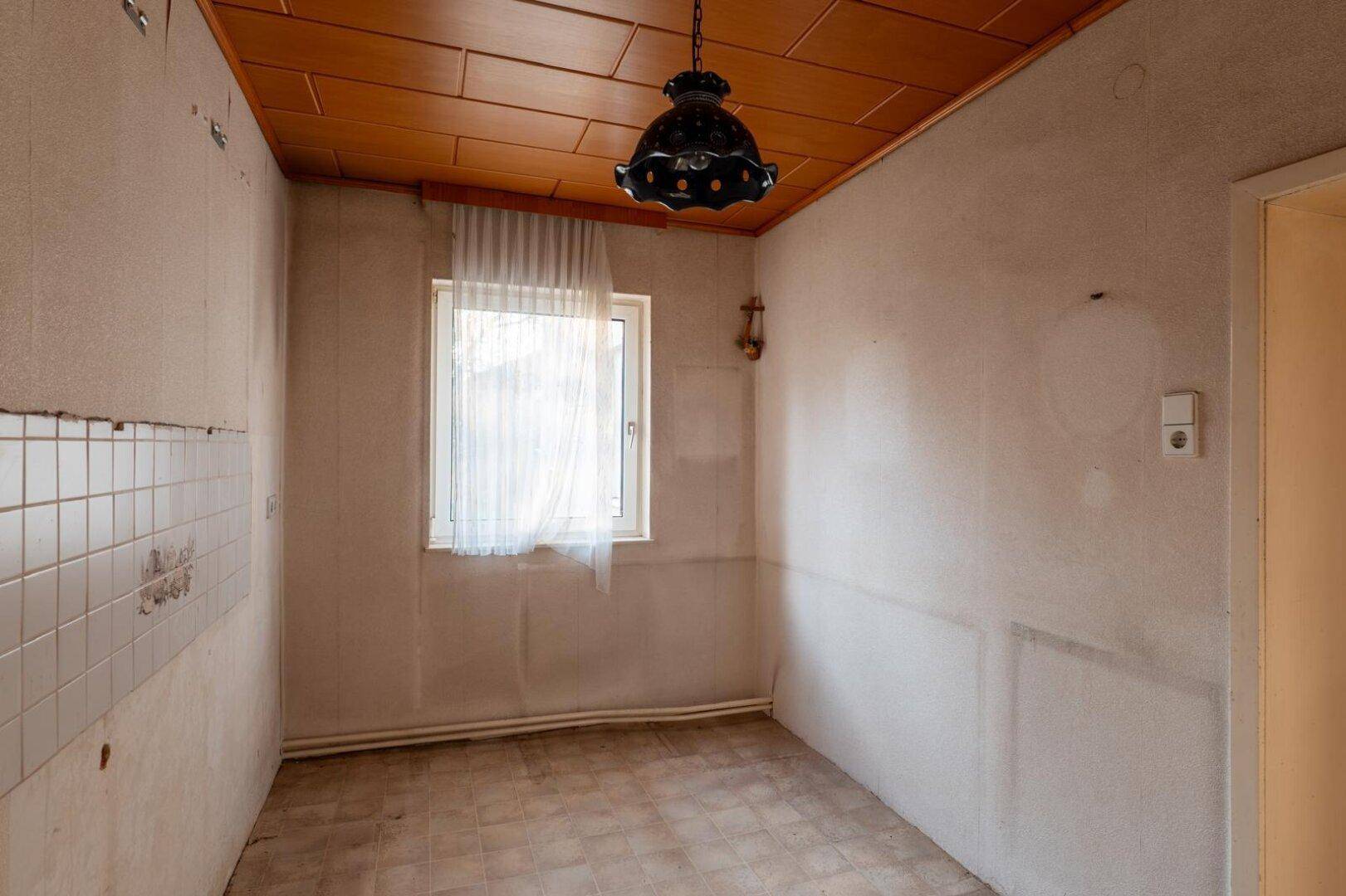 Leere Küche mit Fenster, Holzdecke und alten Fliesen an den Wänden.