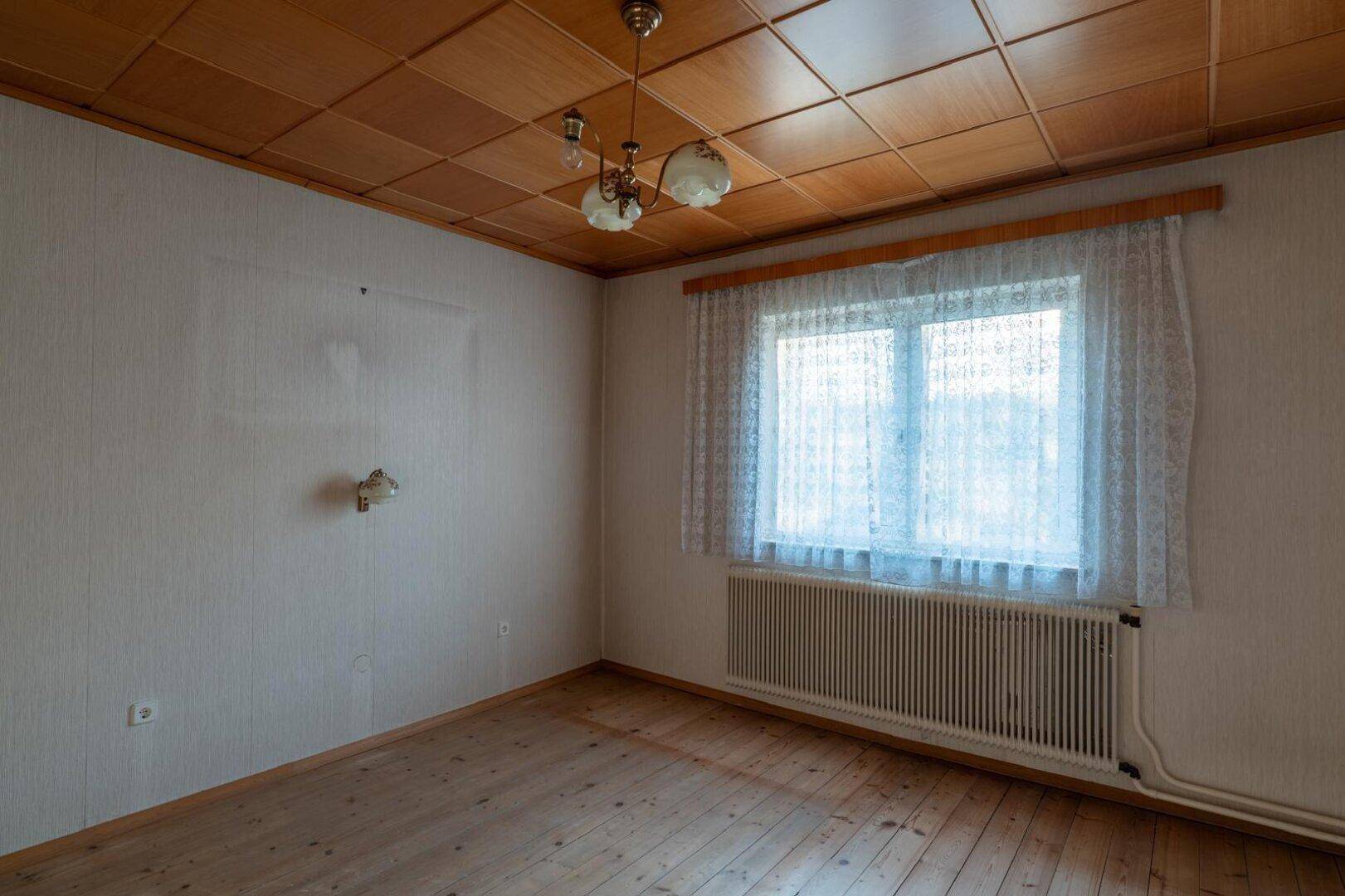 Schlafzimmer mit Holzdielenboden, Holzdecke und einem großen Fenster mit Heizkörper.