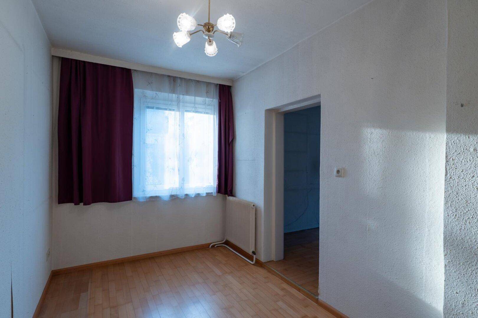 Schlafzimmer mit Laminatboden, Fenster mit Vorhängen und einem Heizkörper darunter.