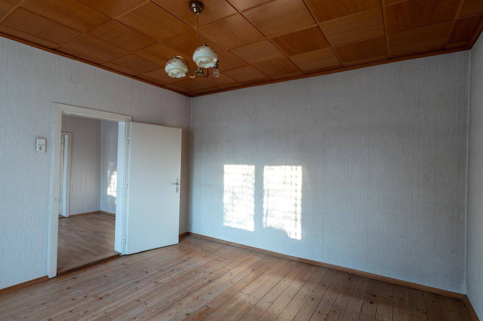 Geräumiges Schlafzimmer mit Holzdielenboden, Holzdecke und einem Durchgang zu einem anderen Raum.