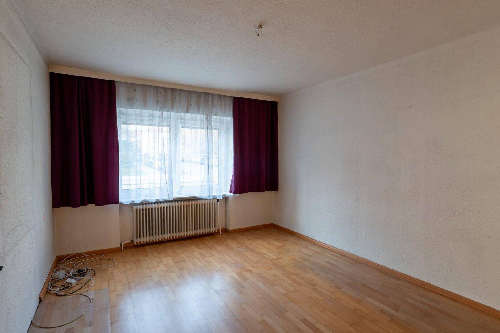 Schlafzimmer mit Laminatboden, Fenster mit Vorhängen und einem Heizkörper.