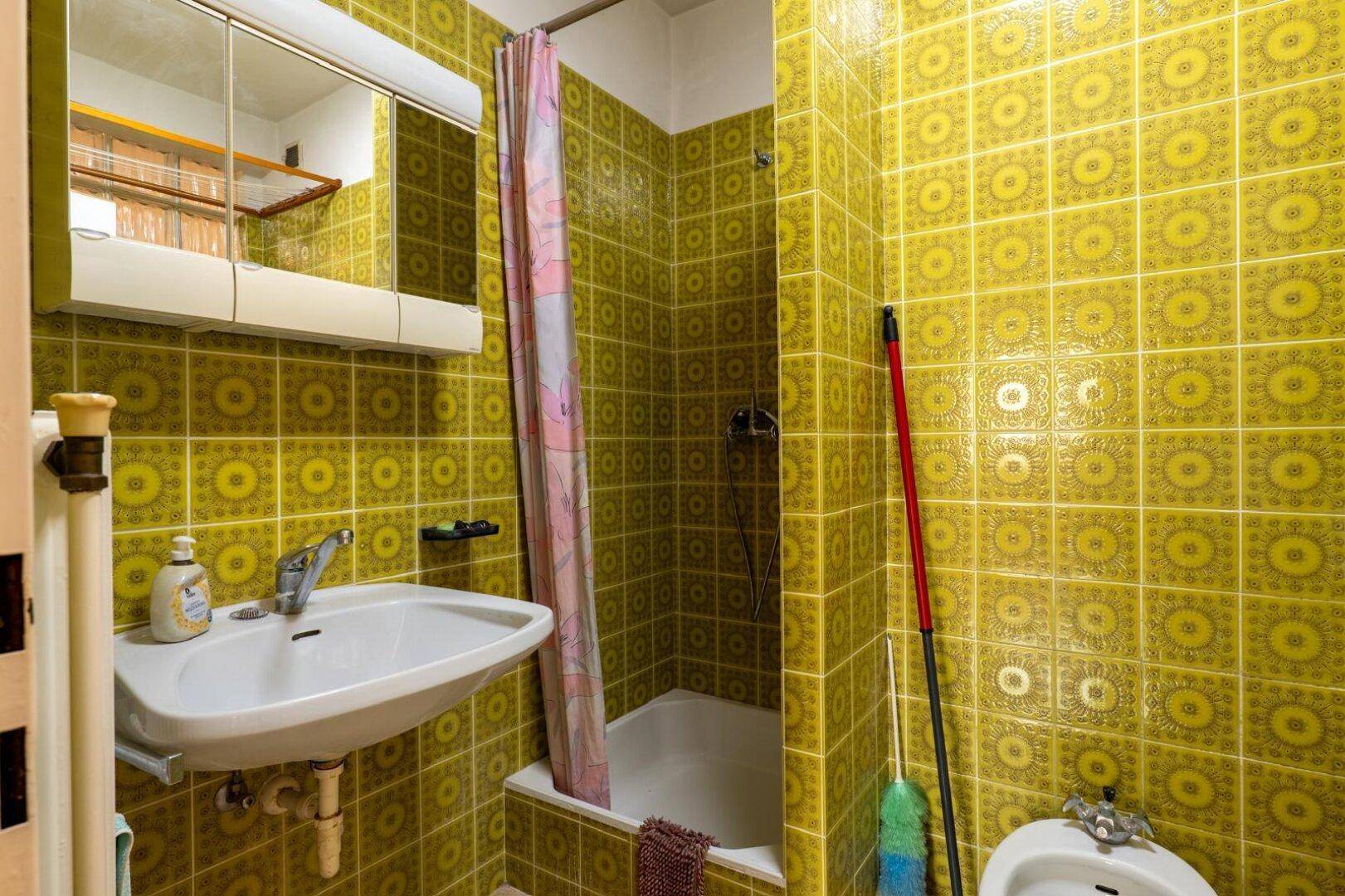 Badezimmer mit auffälligen gelben Fliesen, Badewanne mit Duschvorhang und Waschbecken.
