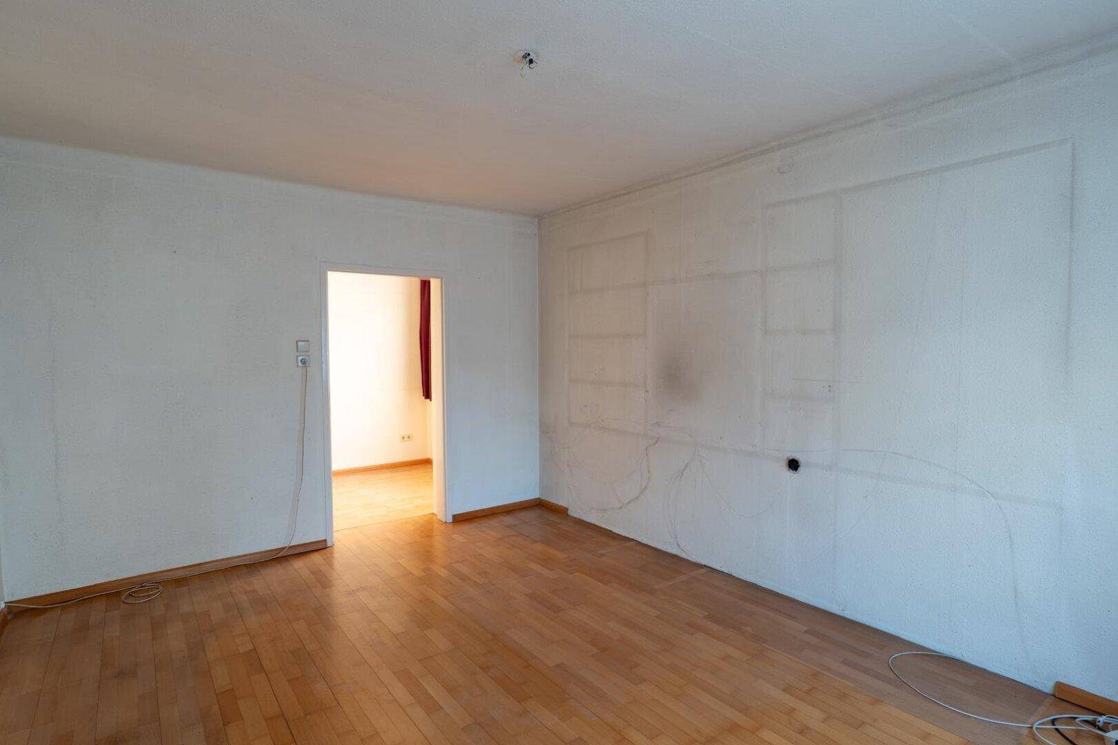 Leeres Zimmer mit Laminatboden und einer Wand, die Spuren von früheren Einbauten zeigt.