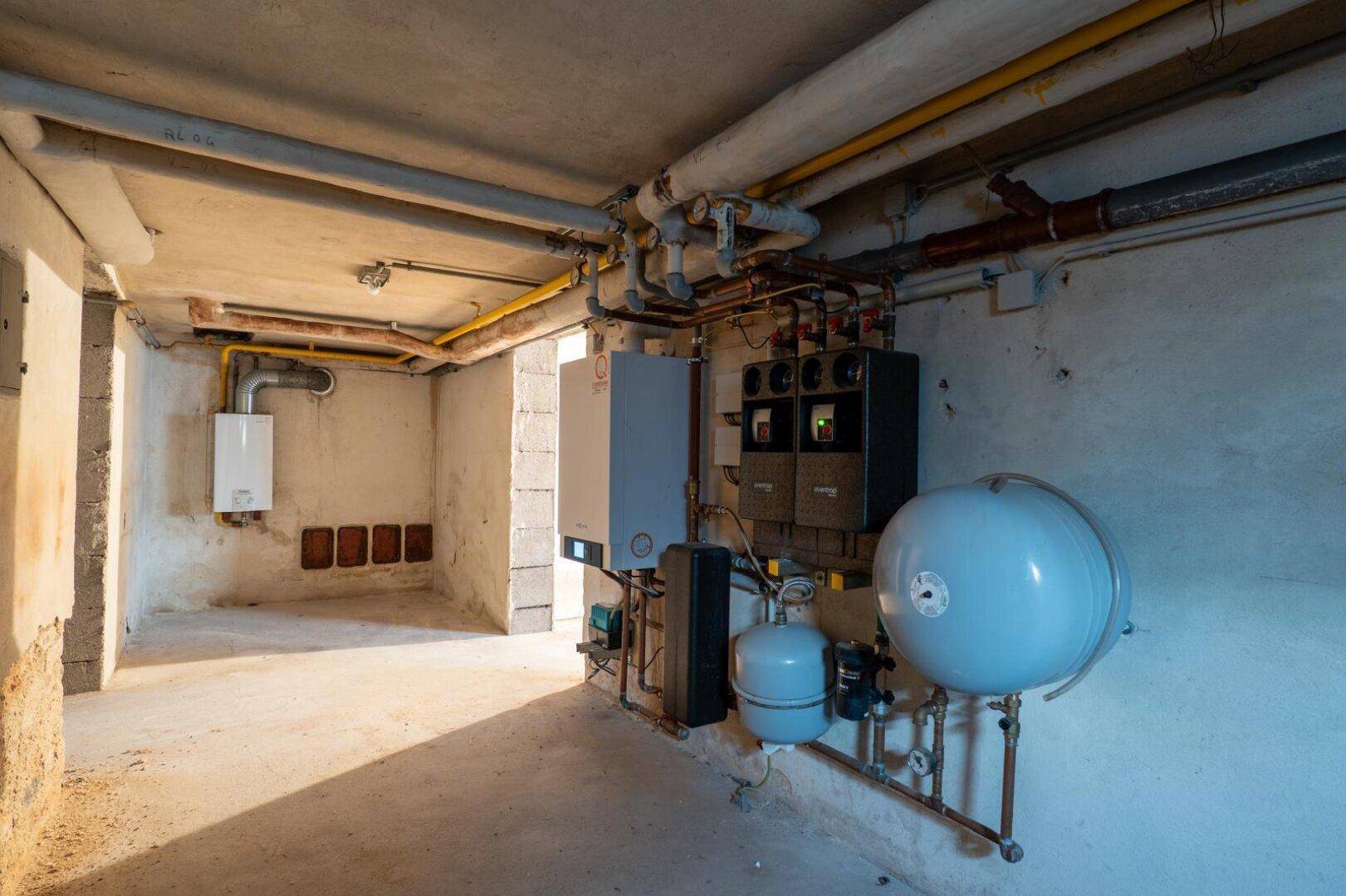 Heizungsraum im Keller mit verschiedenen Rohren, Heizkessel und Warmwasserspeicher.