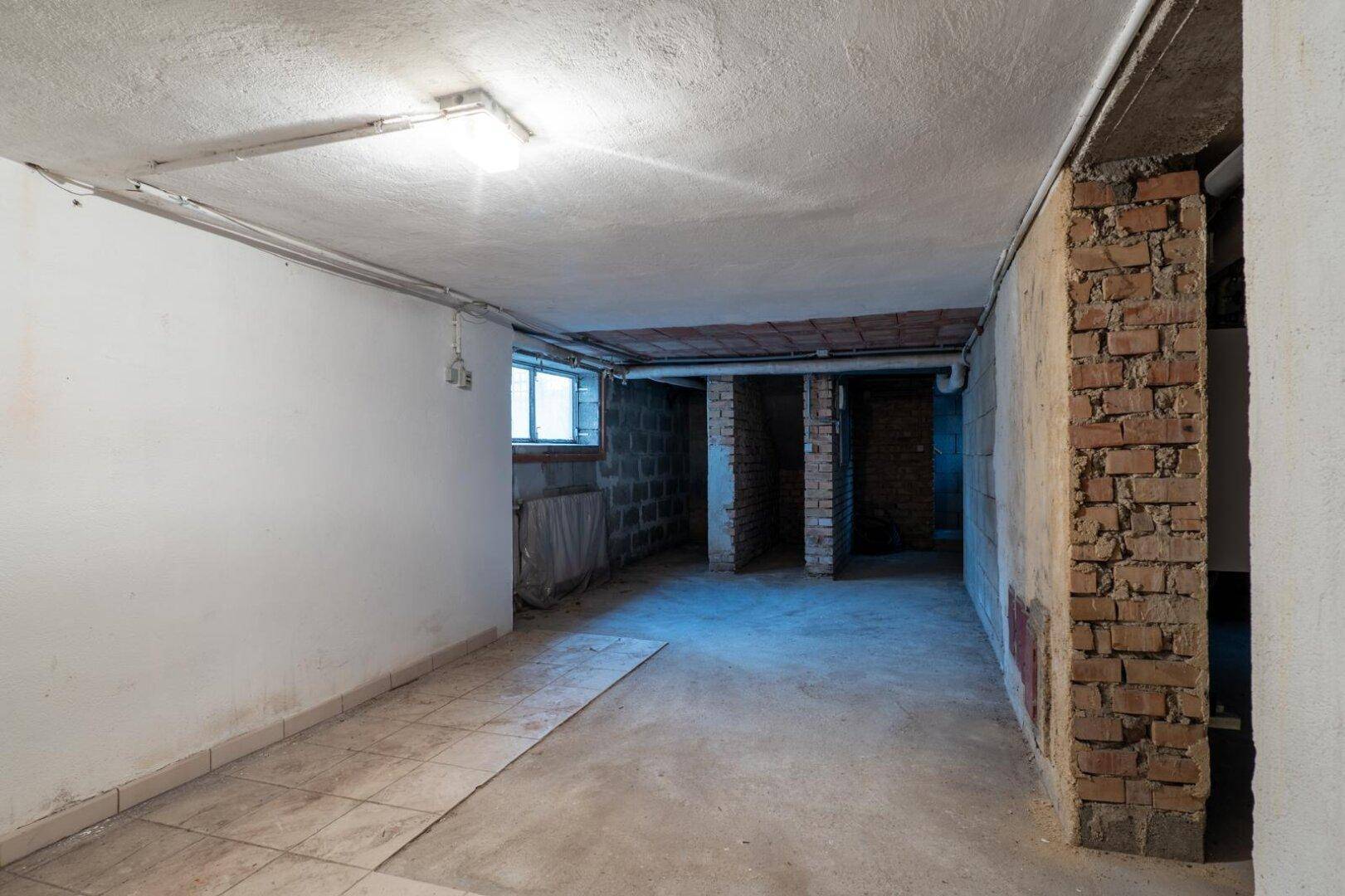 Geräumiger Kellerraum mit Betonboden, unverputzten Wänden und kleinen Fenstern.