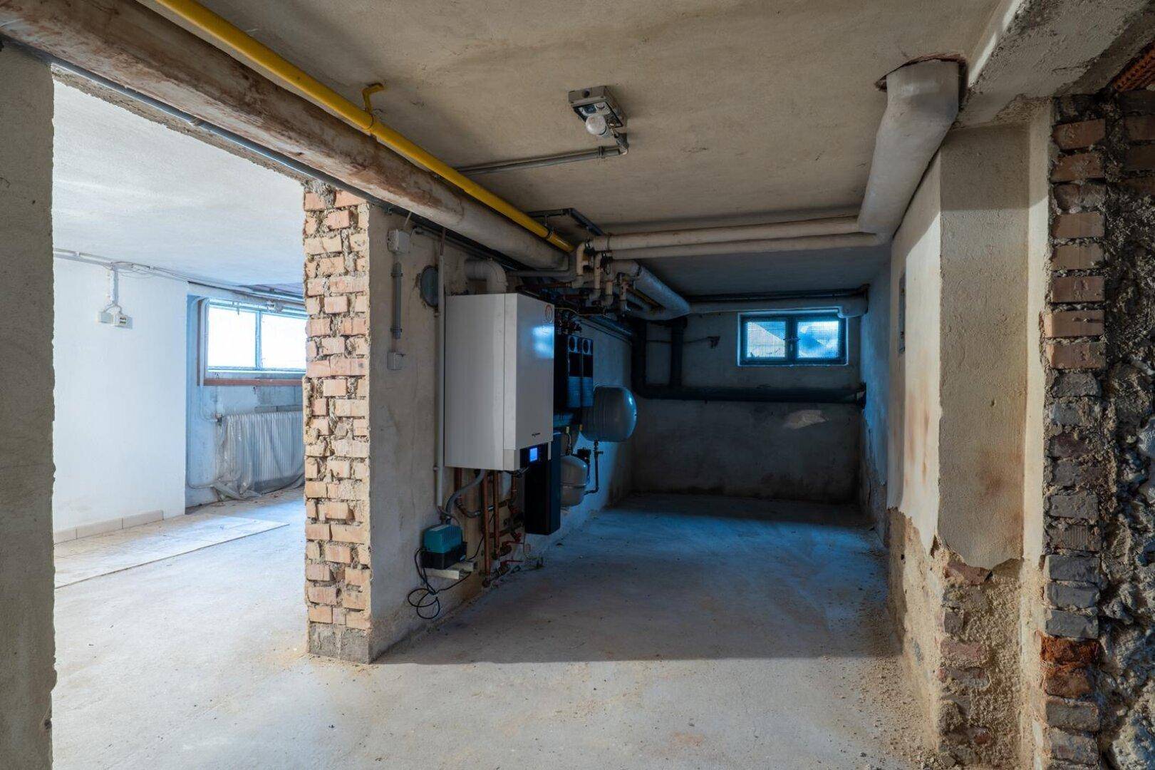 Kellerraum mit Heizungsanlage, freiliegenden Ziegelwänden und kleinen Fenstern.
