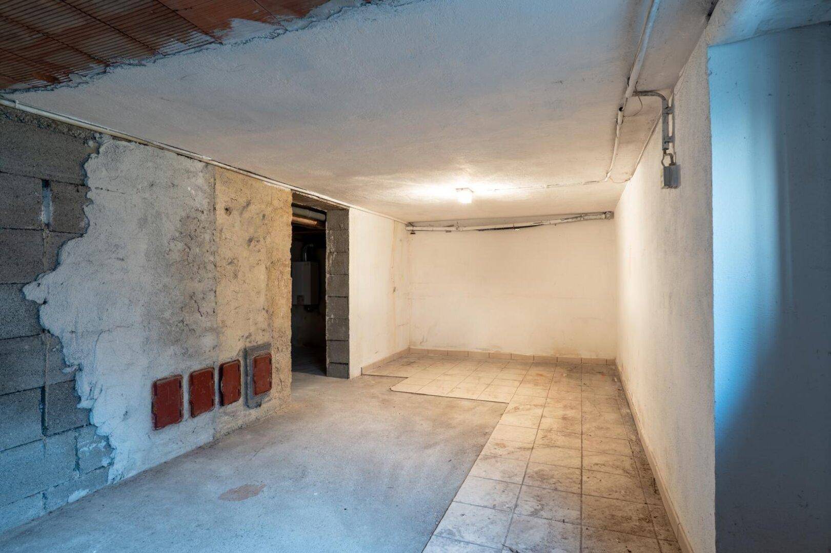 Kellerraum mit Fliesen- und Betonboden, unverputzten Wänden und einer Nische.