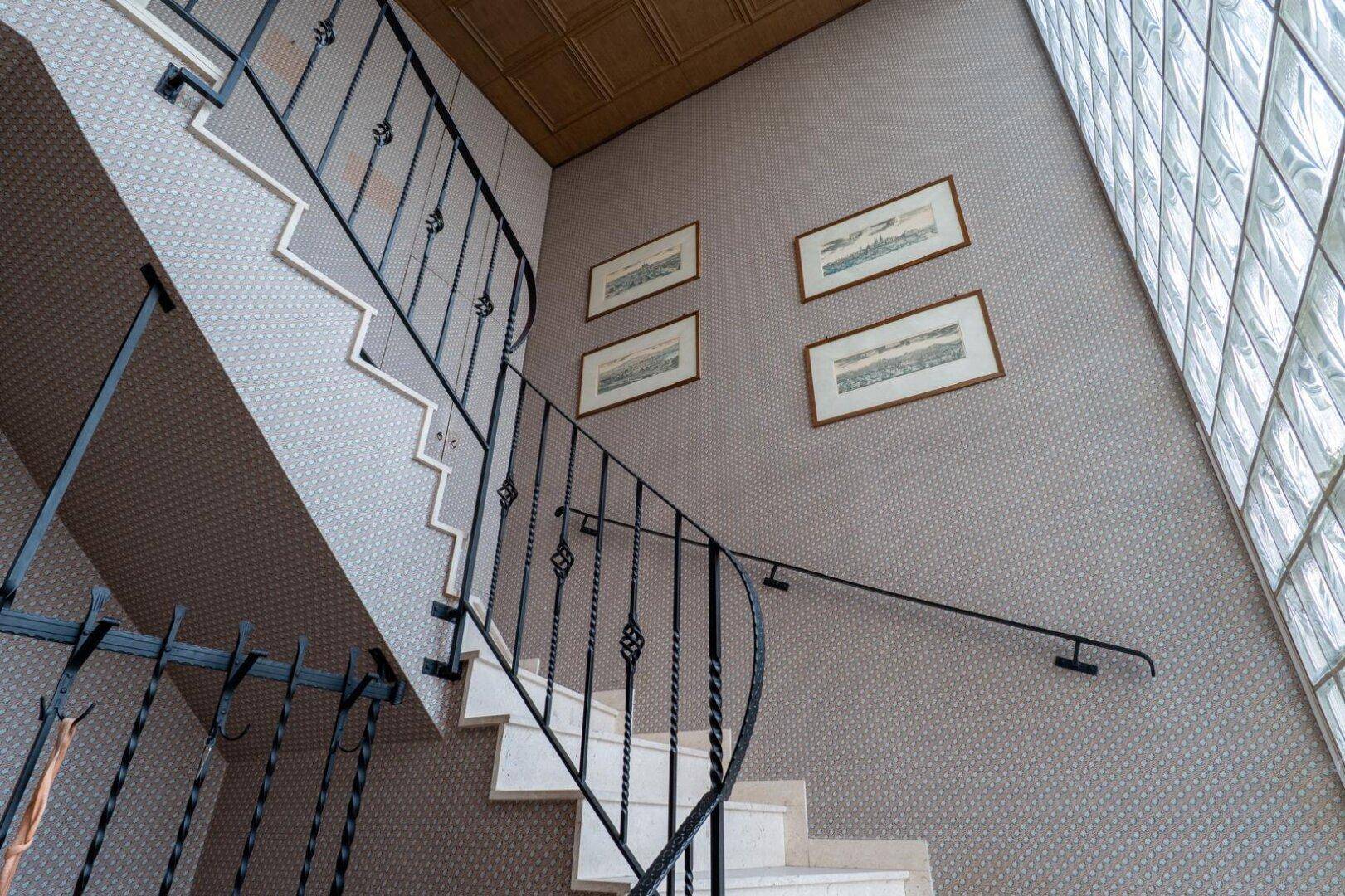 Elegantes Treppenhaus mit Marmorstufen, schmiedeeisernem Geländer und Glasbausteinwand.