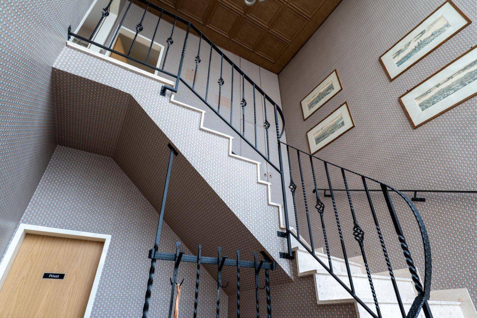 Treppenhaus mit geschwungenem Geländer, Marmorstufen und gemusterter Tapete.