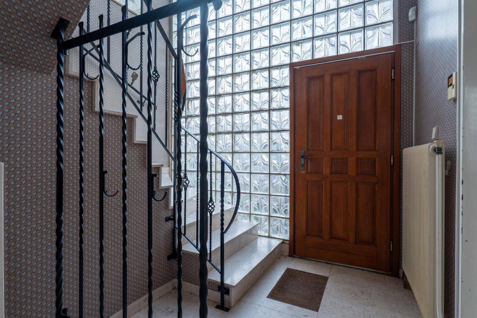 Eingangsbereich mit Marmorboden, Heizkörper und einer Holztür neben der Treppe.