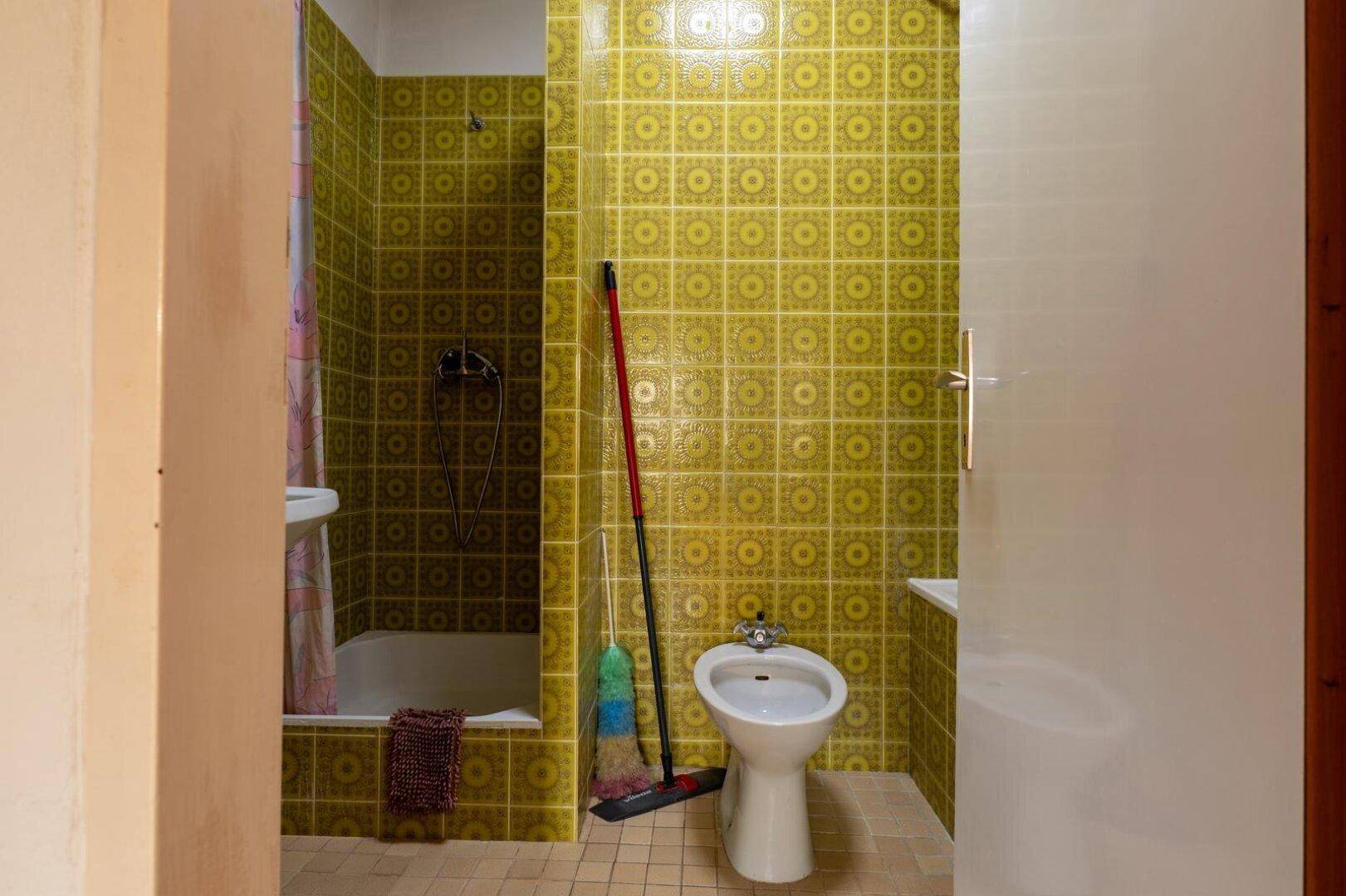 Badezimmer mit gelb-grünen Fliesen, Badewanne mit Duschvorhang und Bidet.