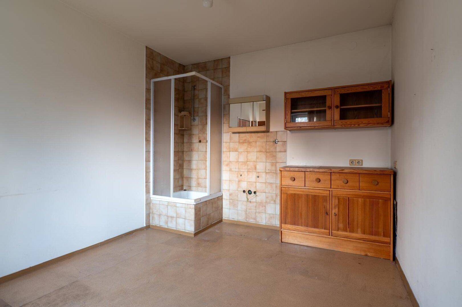 Badezimmer mit Duschkabine, Holzschränken und älteren Fliesen, bereit zur Renovierung.