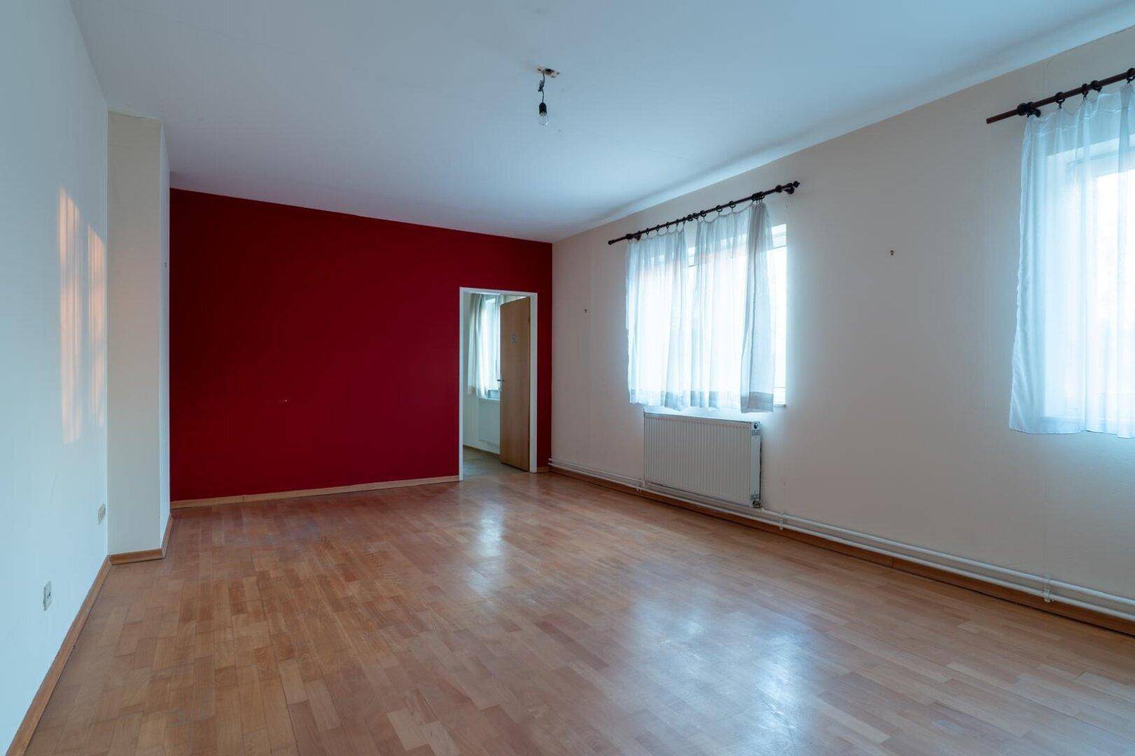 Helles Wohnzimmer mit Parkettboden und einer auffälligen roten Akzentwand.
