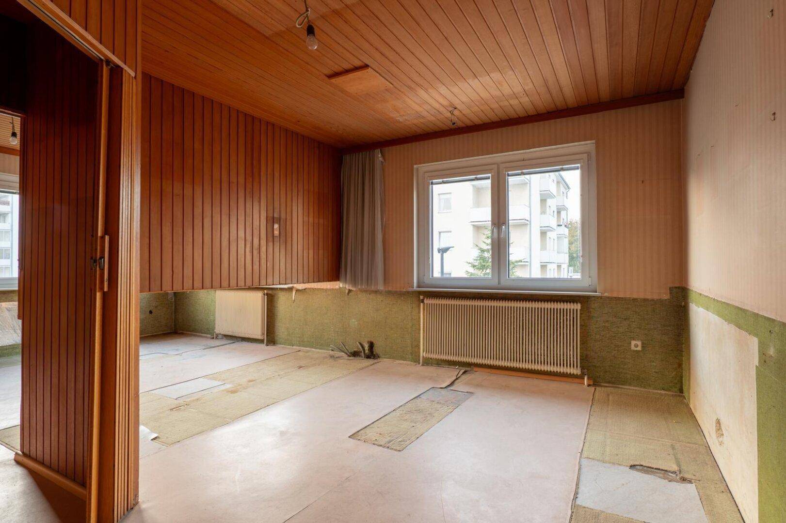 Heller Wohnraum mit Holzvertäfelung und Blick nach draußen, ideal für eine Modernisierung.