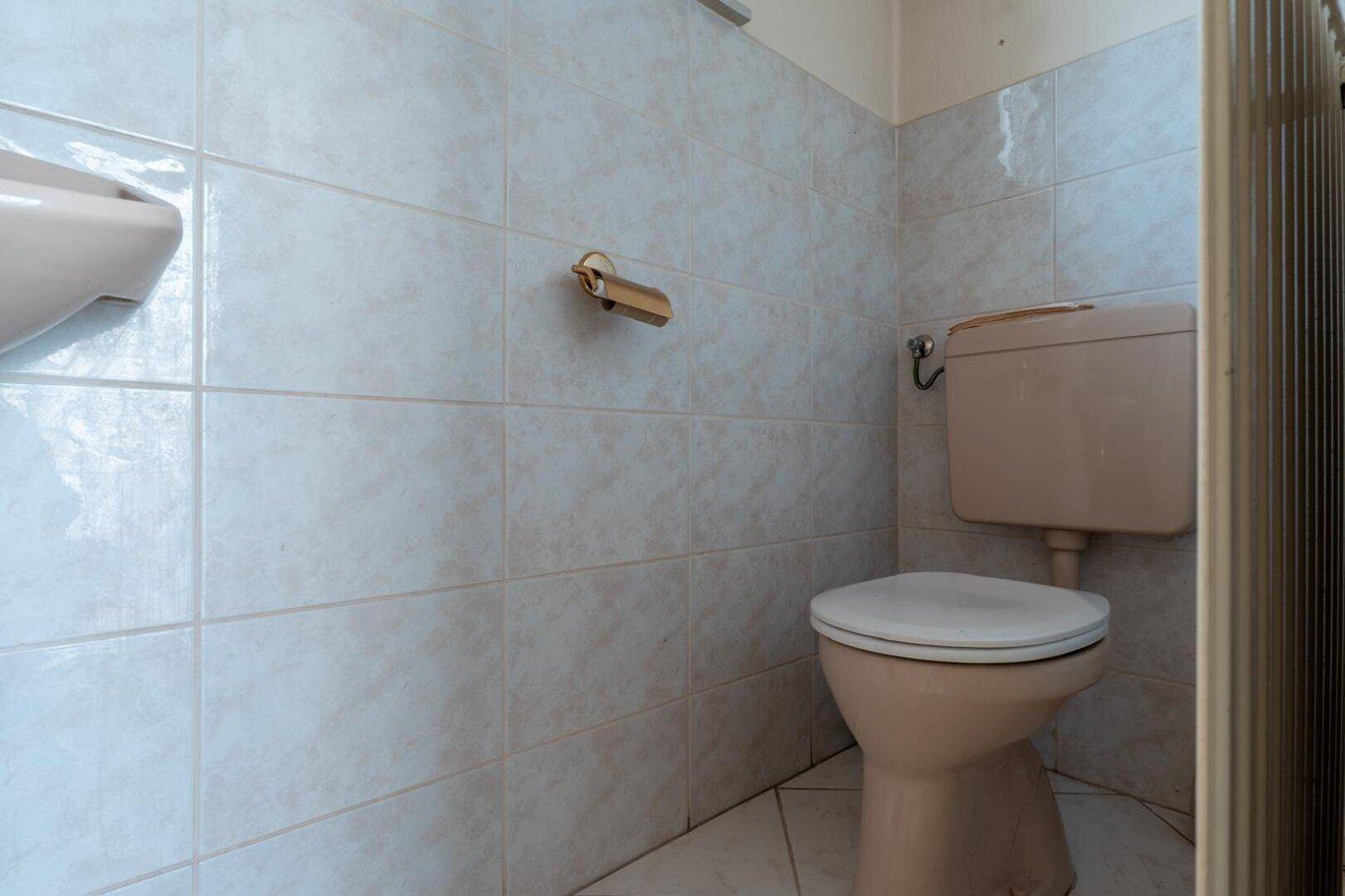 Kleines WC mit hellblauen Fliesen und beigefarbener Toilette, im Stil der 80er Jahre.