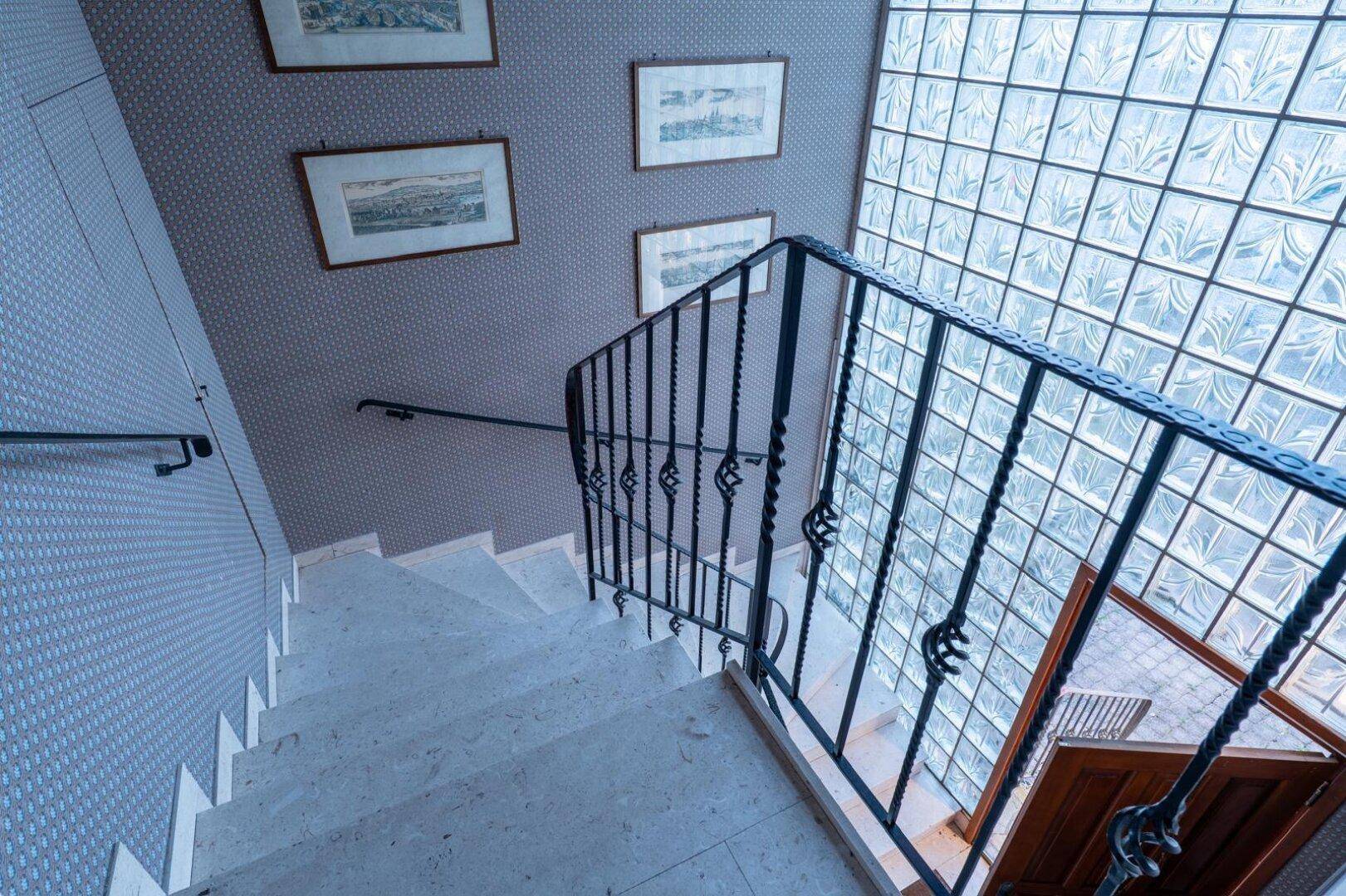 Elegantes Treppenhaus mit Marmorstufen, schmiedeeisernem Geländer und Glasbausteinwand.