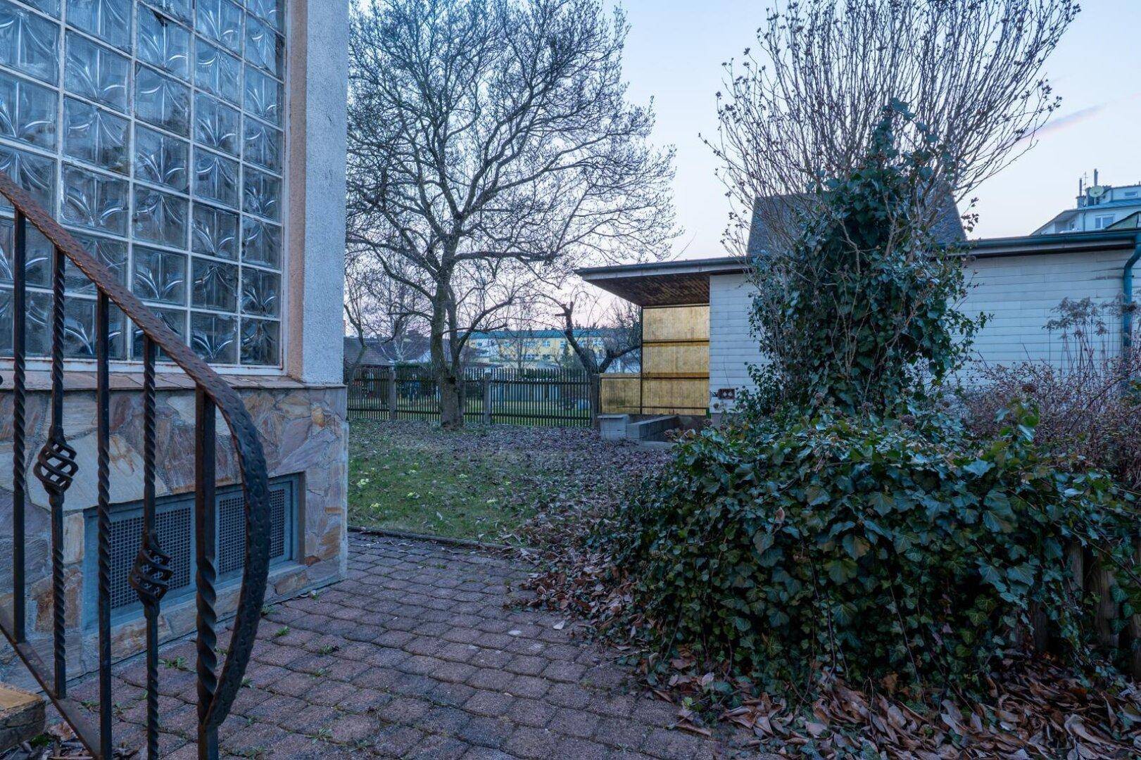 Außenbereich mit gepflastertem Weg, üppiger Bepflanzung und Blick in den Garten.