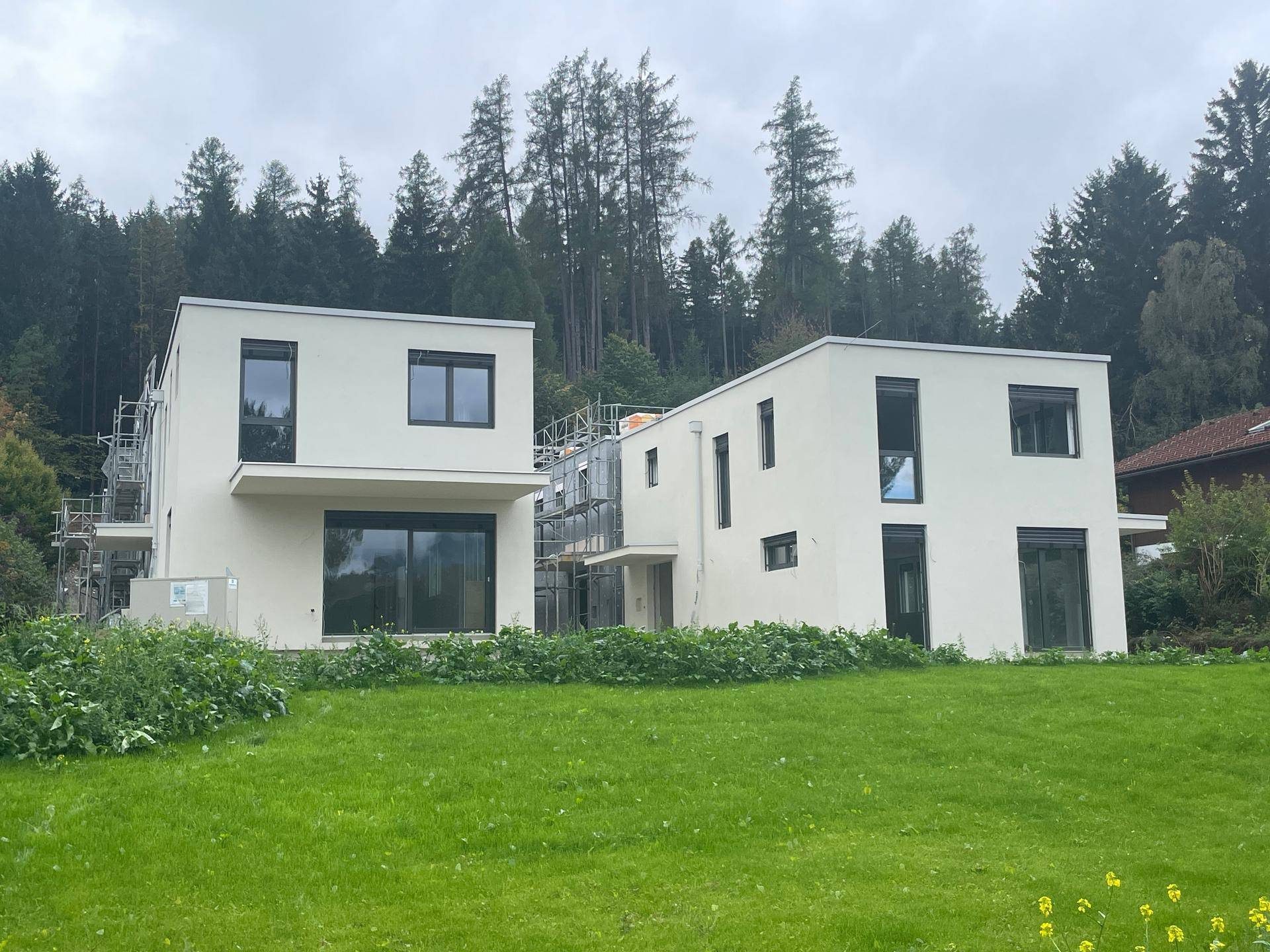 Zwei moderne Häuser im Bau mit Gerüst und grüner Wiese im Vordergrund.