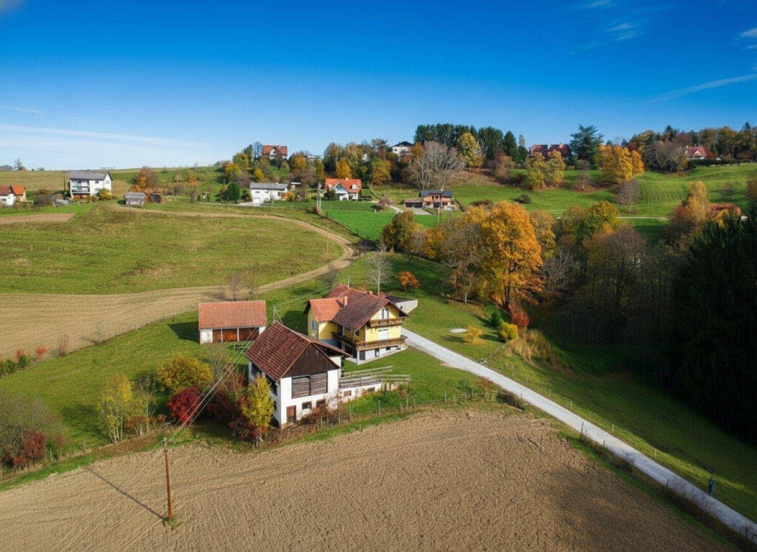 Ländliches Anwesen mit mehreren Gebäuden und einem Feldweg, umgeben von grünen Hügeln und Herbstbäumen.
