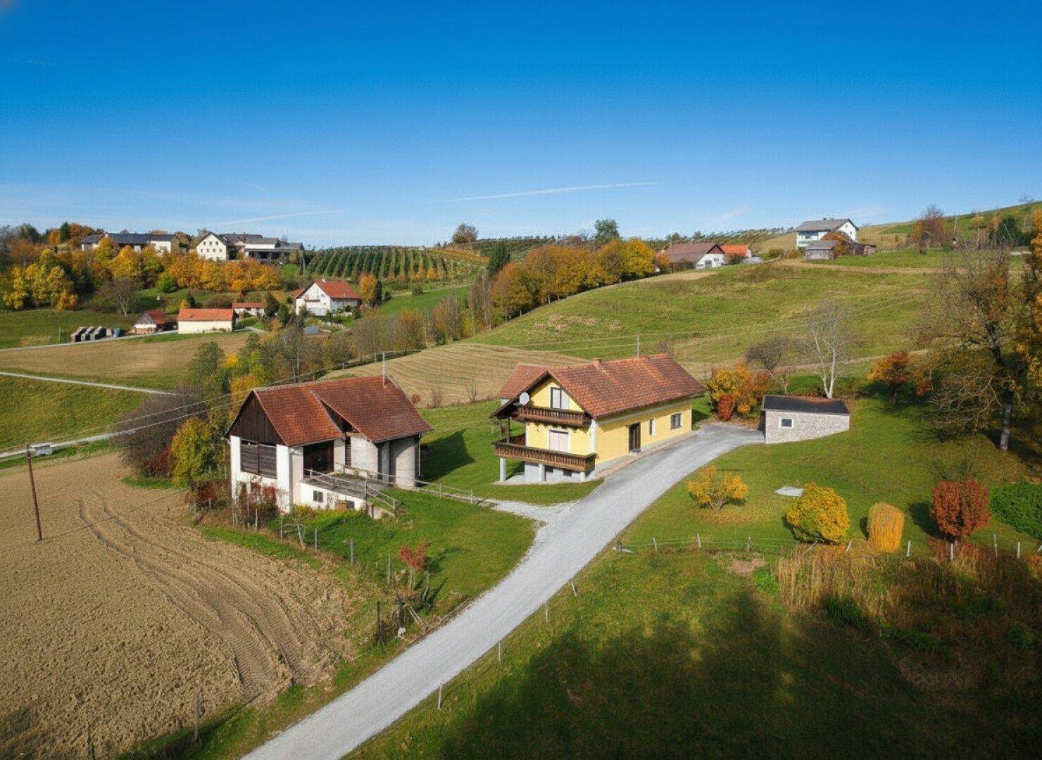 Zwei ländliche Häuser mit roten Dächern und Balkonen, eingebettet in eine hügelige Herbstlandschaft.