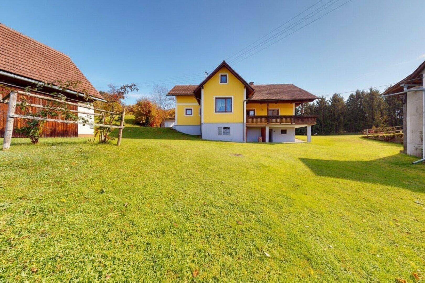 Freistehendes gelbes Haus mit Balkon und großem Gartenbereich, umgeben von Bäumen und Natur.