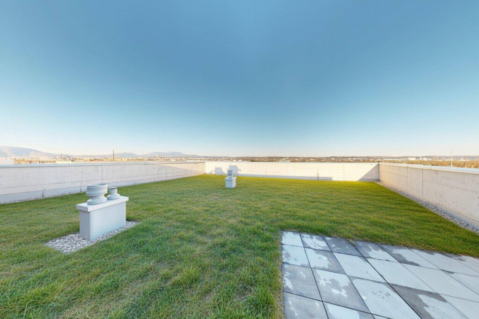 Weitläufige, unmöblierte Dachterrasse mit Rasenfläche und weitem Blick über die Umgebung.