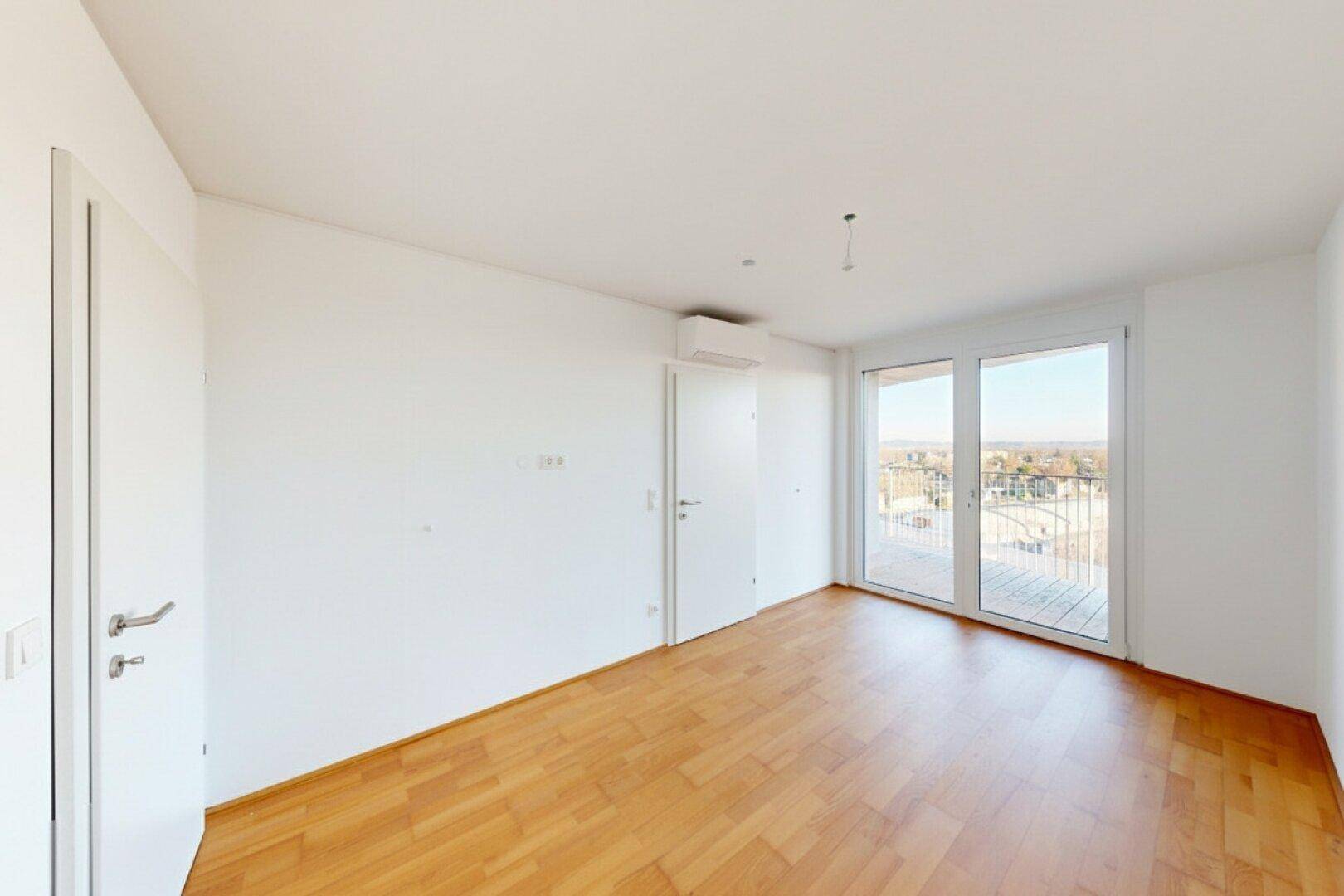 Geräumiges Schlafzimmer mit Holzboden, Klimaanlage und Zugang zu einem sonnigen Balkon.