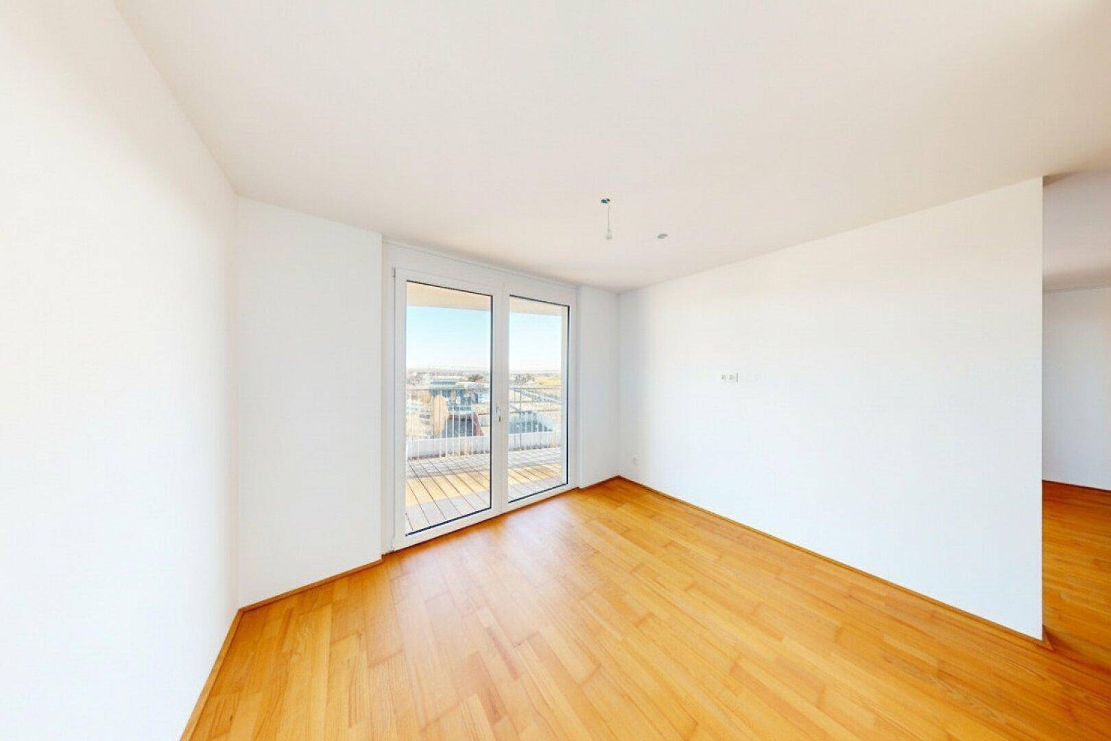 Heller Raum mit Holzboden und großen Fenstern, die viel Tageslicht hereinlassen und einen Balkonblick bieten.