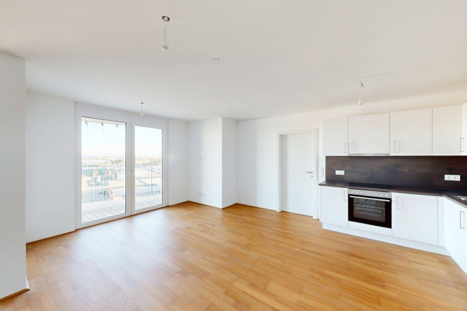 Heller, offener Wohnbereich mit integrierter Küche, Holzboden und Zugang zu einem Balkon.
