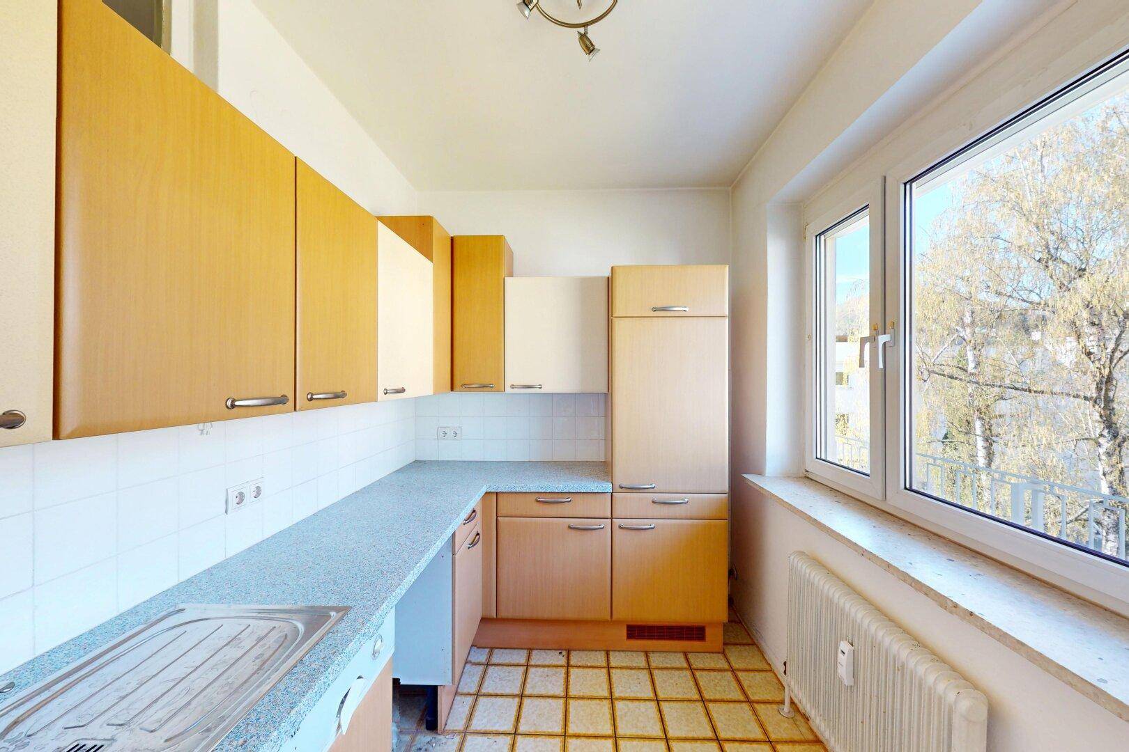 Funktionale Küche mit hellen Holzschränken, Fliesenboden und Fenster mit Blick ins Grüne.