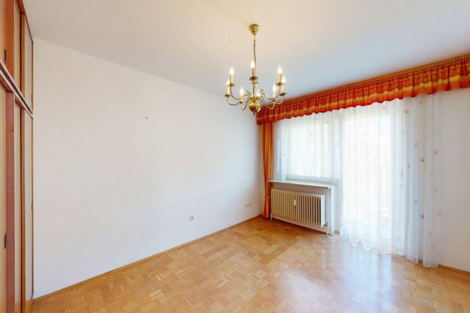 Schlafzimmer mit Parkettboden, großem Fenster und einem klassischen Kronleuchter.