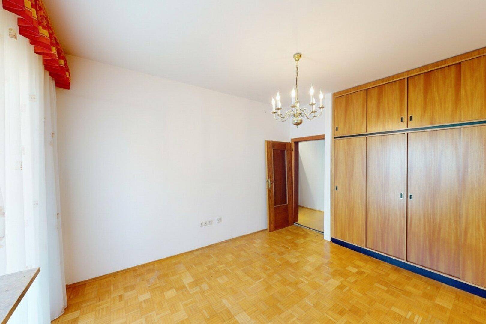 Schlafzimmer mit Einbauschränken aus Holz und Parkettboden, gut beleuchtet.