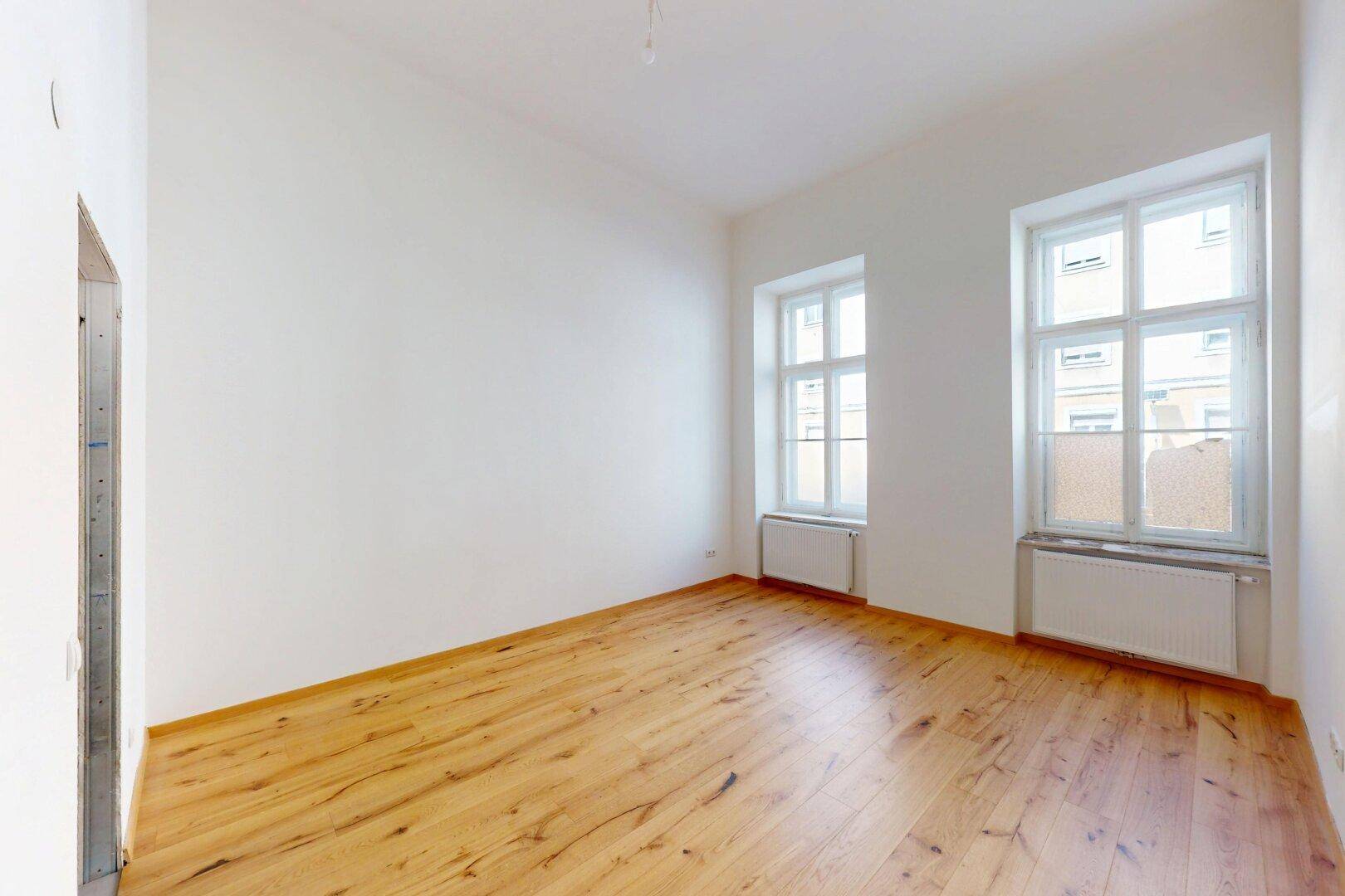 Heller, leerer Raum mit weiß gestrichenen Wänden und neuem Holzboden.