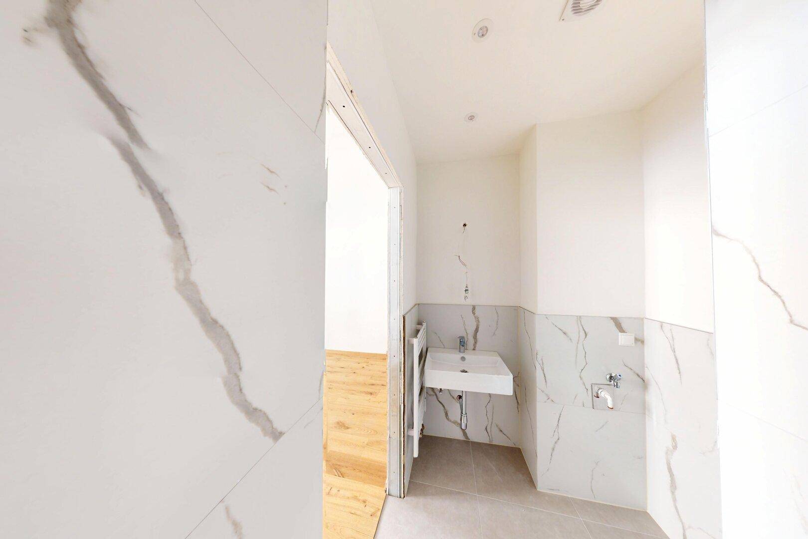 Badezimmer im Bau mit Wandwaschbecken und stilvollen Fliesen in Marmoroptik.