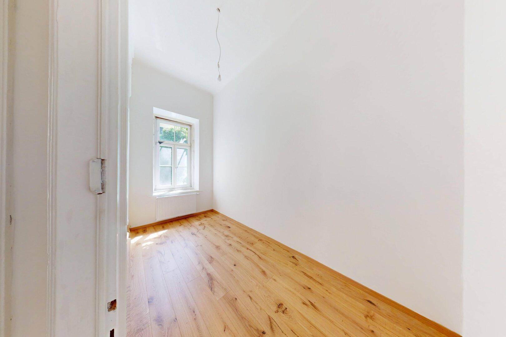Kleiner, heller Raum mit Holzboden und einem Fenster, ideal als Schlaf- oder Arbeitszimmer.